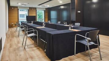 Un salón de conferencias con una larga mesa, sillas y una pantalla de televisión.