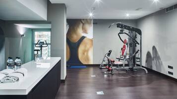 Een fitnessruimte met trainingsapparatuur, een balie met handdoeken en waterflessen, en een grote poster aan de muur.