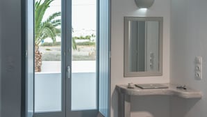 Une salle de bain avec une porte coulissante en verre, un miroir, un petit lavabo et un tabouret.