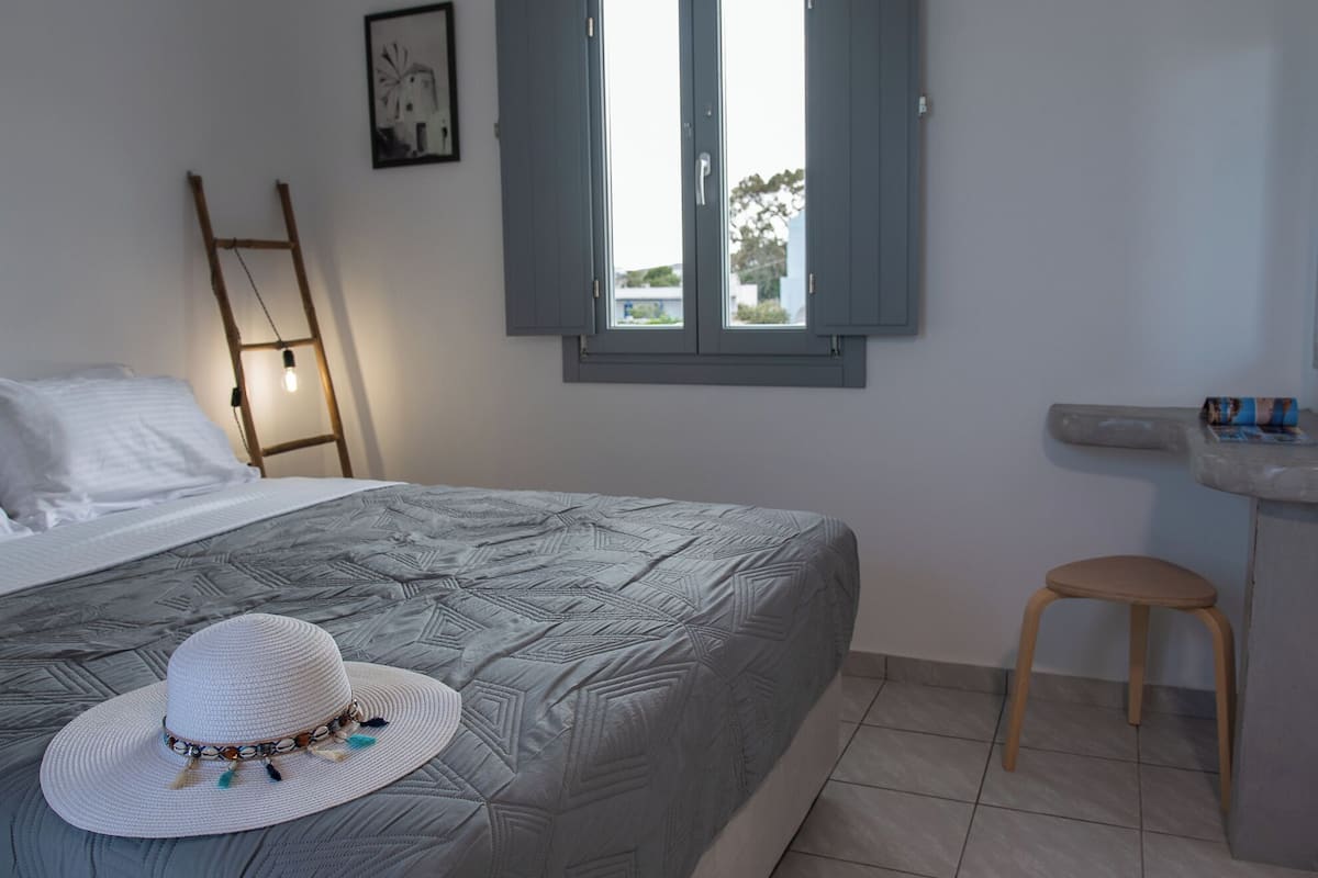 Quarto com cama, janela, escada, banquinho e prateleira fixada na parede.