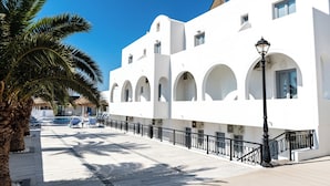Un bâtiment blanc doté de fenêtres en arc de cercle et d’une rambarde noire le long du trottoir.
