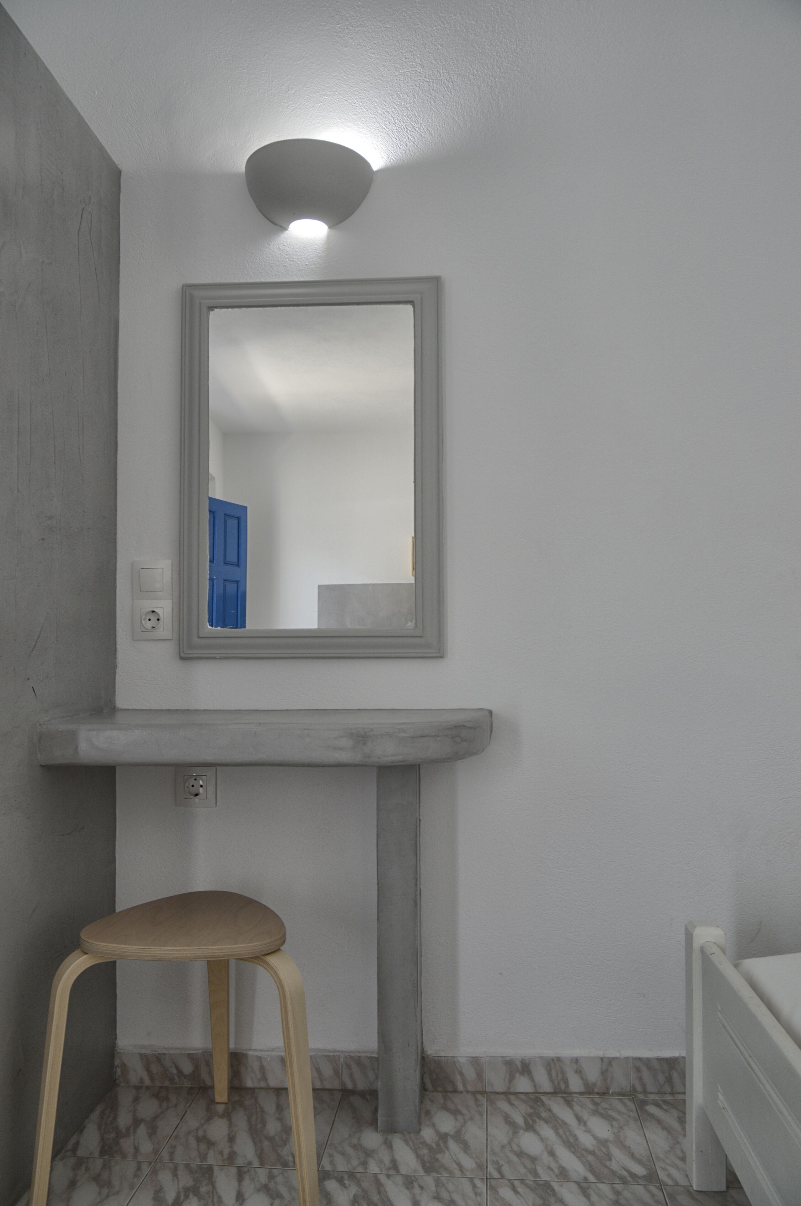 A bathroom with a marble floor, a wooden stool, a white radiator, and a mirror with a blue door reflection.
