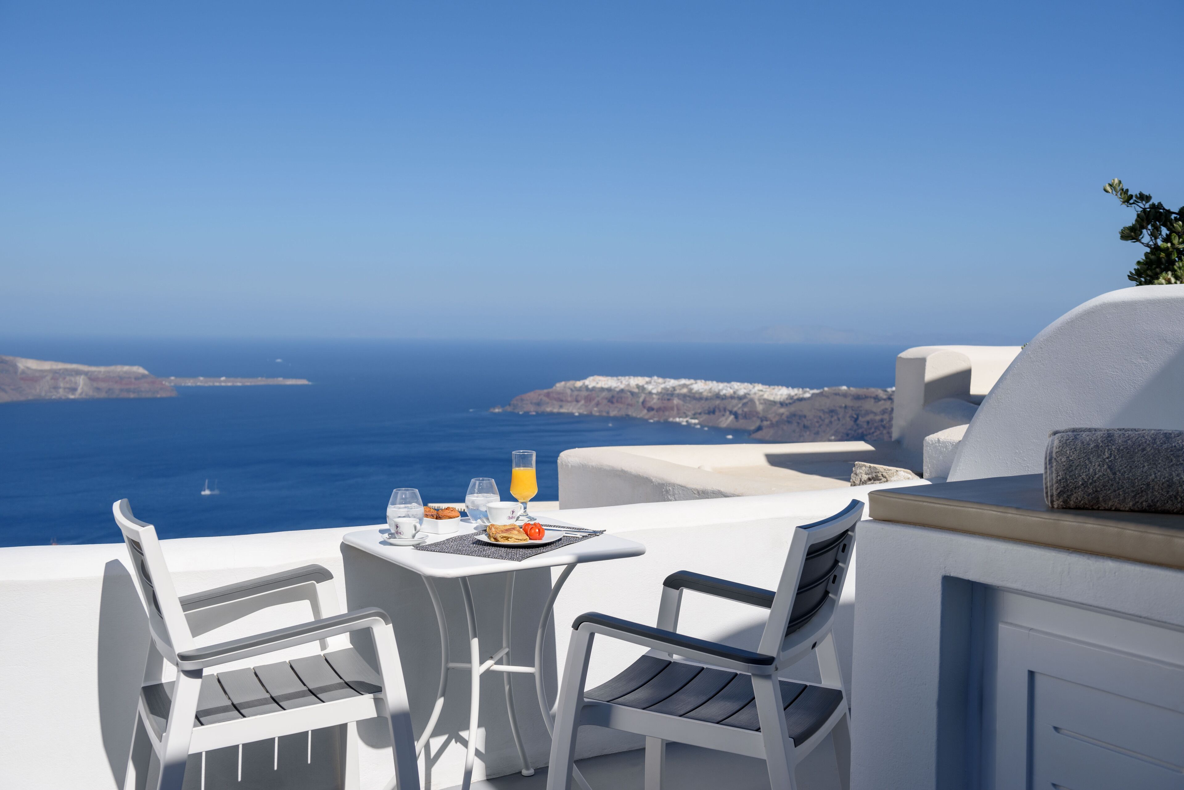 Ein Tisch mit zwei Stühlen, ein Glas Orangensaft und ein Teller Essen auf einer Terrasse mit Meerblick.
