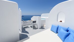 A white room with a bed, a table, and two chairs. There is a view of the ocean. - Abyssanto Suites & Spa (Santorini)