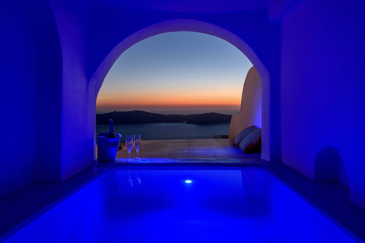 A pool area with a view of the sea at dusk, a potted plant, and two glasses.