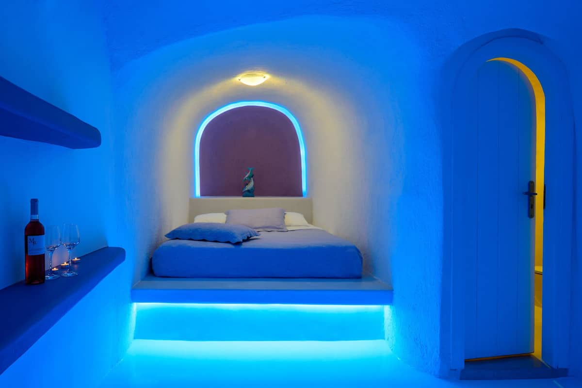 A modern bedroom with a bed, a bottle of wine, and glasses on a shelf.