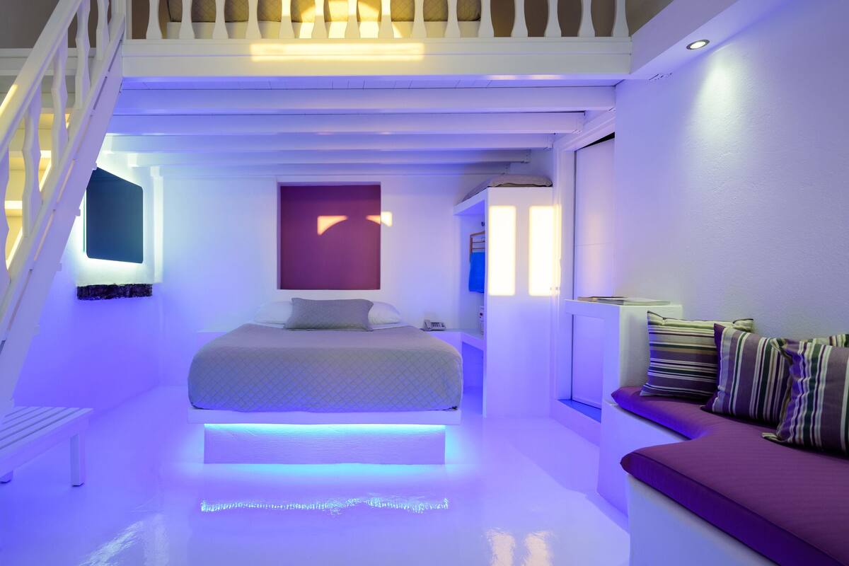 A modern bedroom with a loft-style bed, a white staircase, and a built-in bench with cushions.