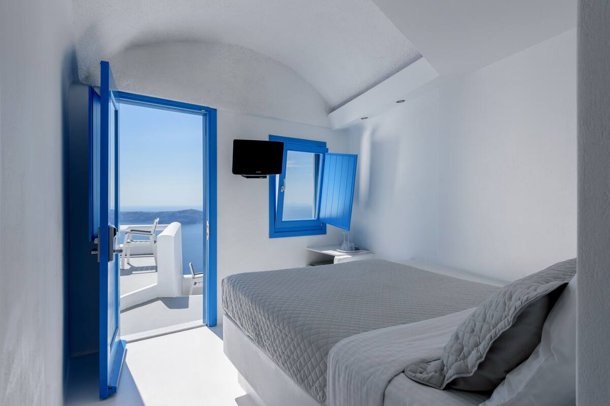 A modern bedroom with a large bed, a TV, and a view of the sea.