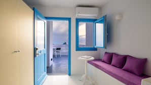 A room with a purple sofa, a small round table, and a door leading to another room. - Abyssanto Suites & Spa (Santorini)