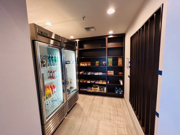 Un couloir avec un réfrigérateur rempli de boissons et d’en-cas, ainsi que des étagères contenant des aliments emballés.