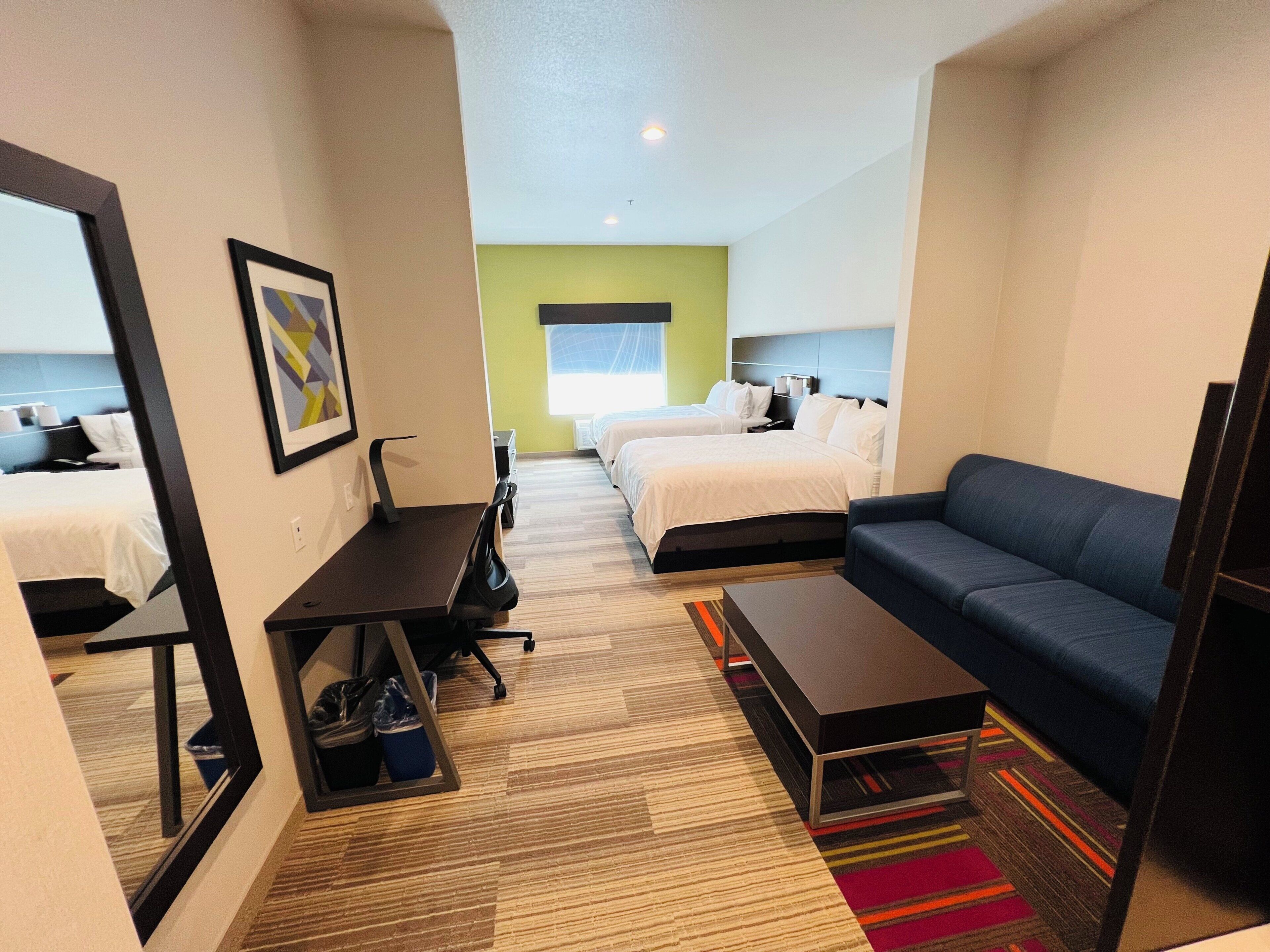 Habitación de hotel con cama, sofá, escritorio y espejo.