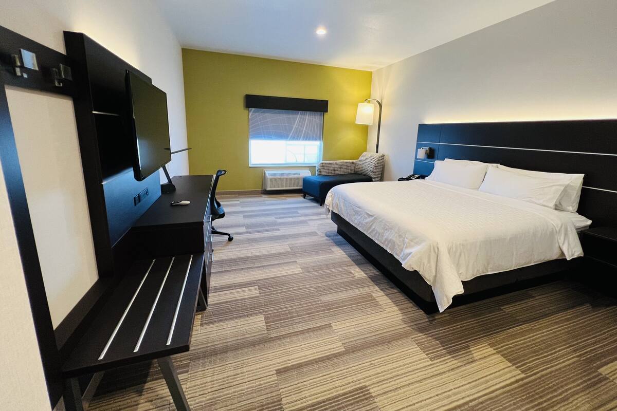 A hotel room with a bed, desk, chair, TV, and a window with blinds.
