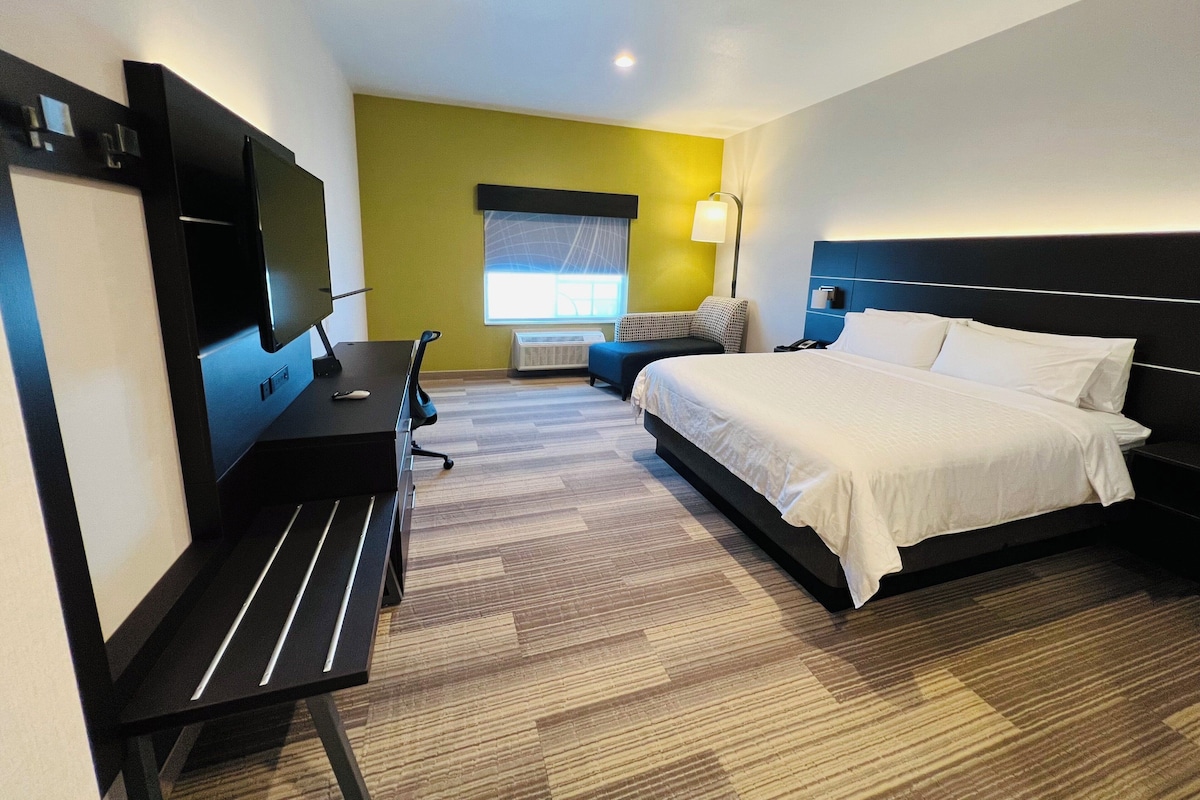 Une chambre d’hôtel équipée d’un lit, d’un bureau, d’une chaise, d’une télévision et d’une fenêtre avec des stores.