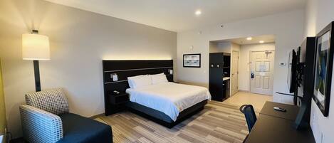 A hotel room with a bed, a desk, a chair, a lamp, and a TV.