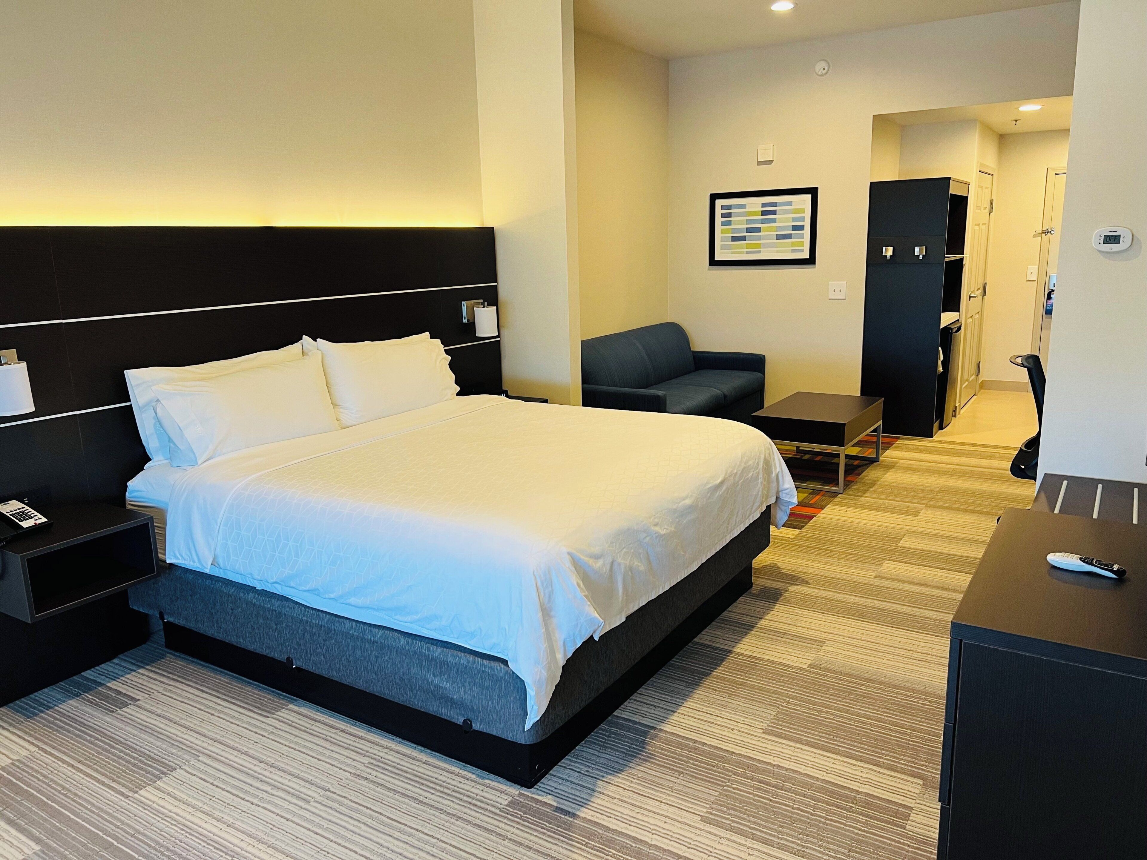 Ein Hotelzimmer mit einem großen Bett, einem Nachttisch, einem Sessel, einem kleinen Tisch und einem Schreibtisch.