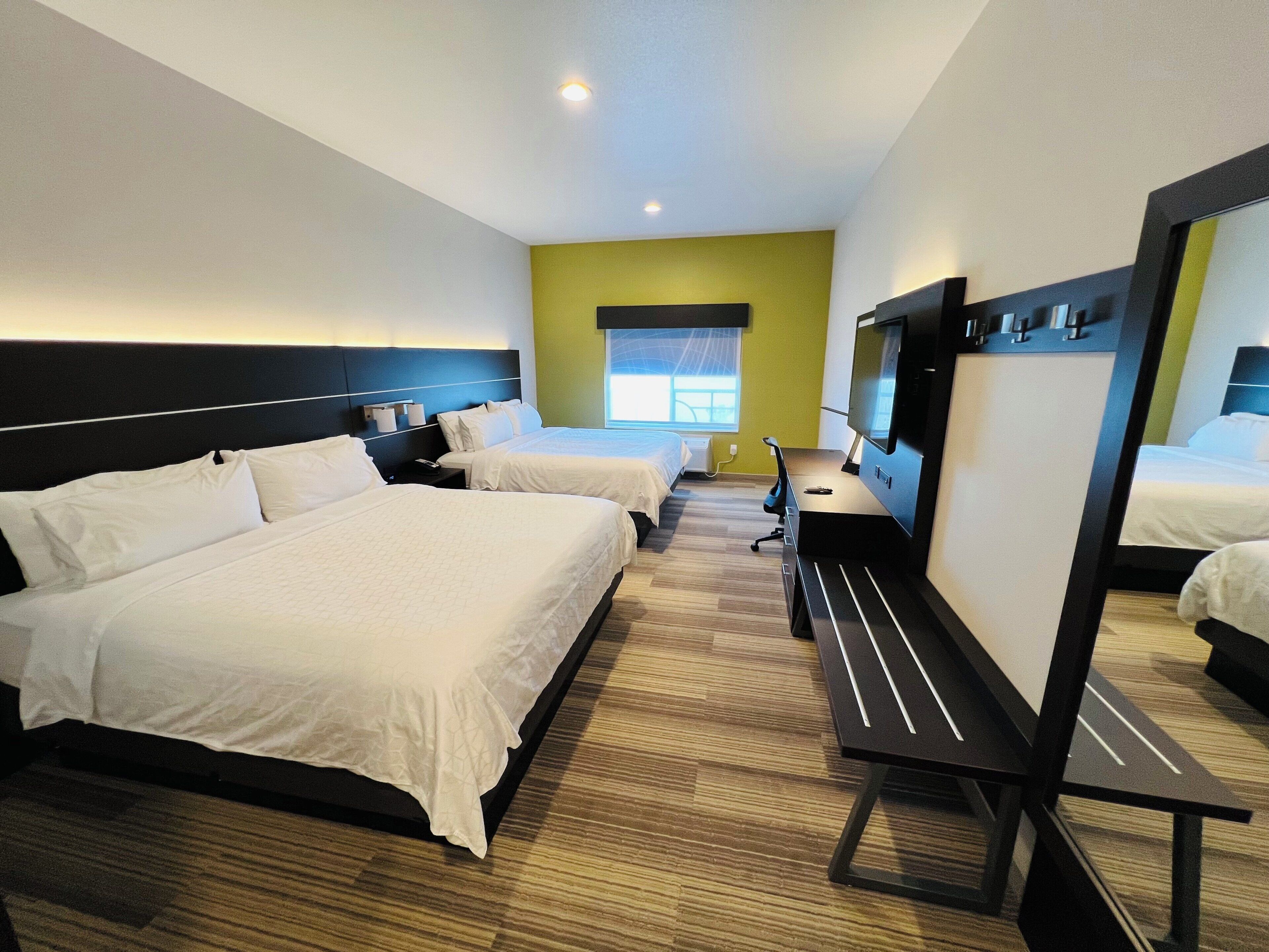 Une chambre d’hôtel avec deux lits, un bureau, une chaise, un téléviseur à écran plat et un grand miroir.