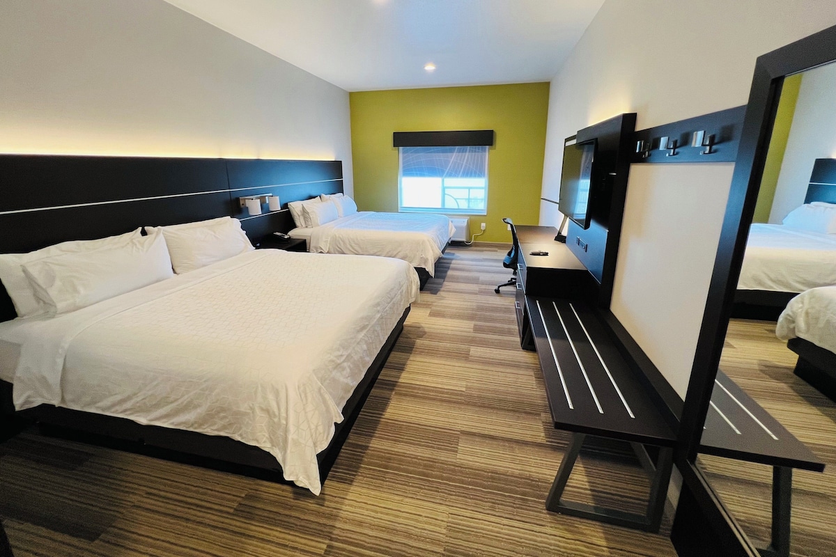 Une chambre d’hôtel avec deux lits, un bureau, une chaise, un téléviseur à écran plat et un grand miroir.