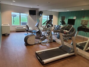 A gym with treadmills, elliptical machines, and stationary bikes, large windows, and a green wall.