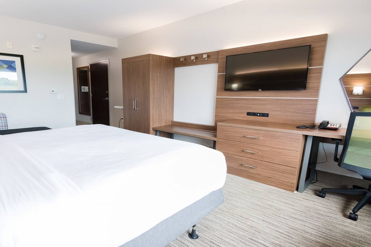 A hotel room with a bed, a desk with a computer, a TV, and a wardrobe.