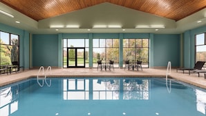 A swimming pool with a wooden ceiling, large windows, and outdoor seating.