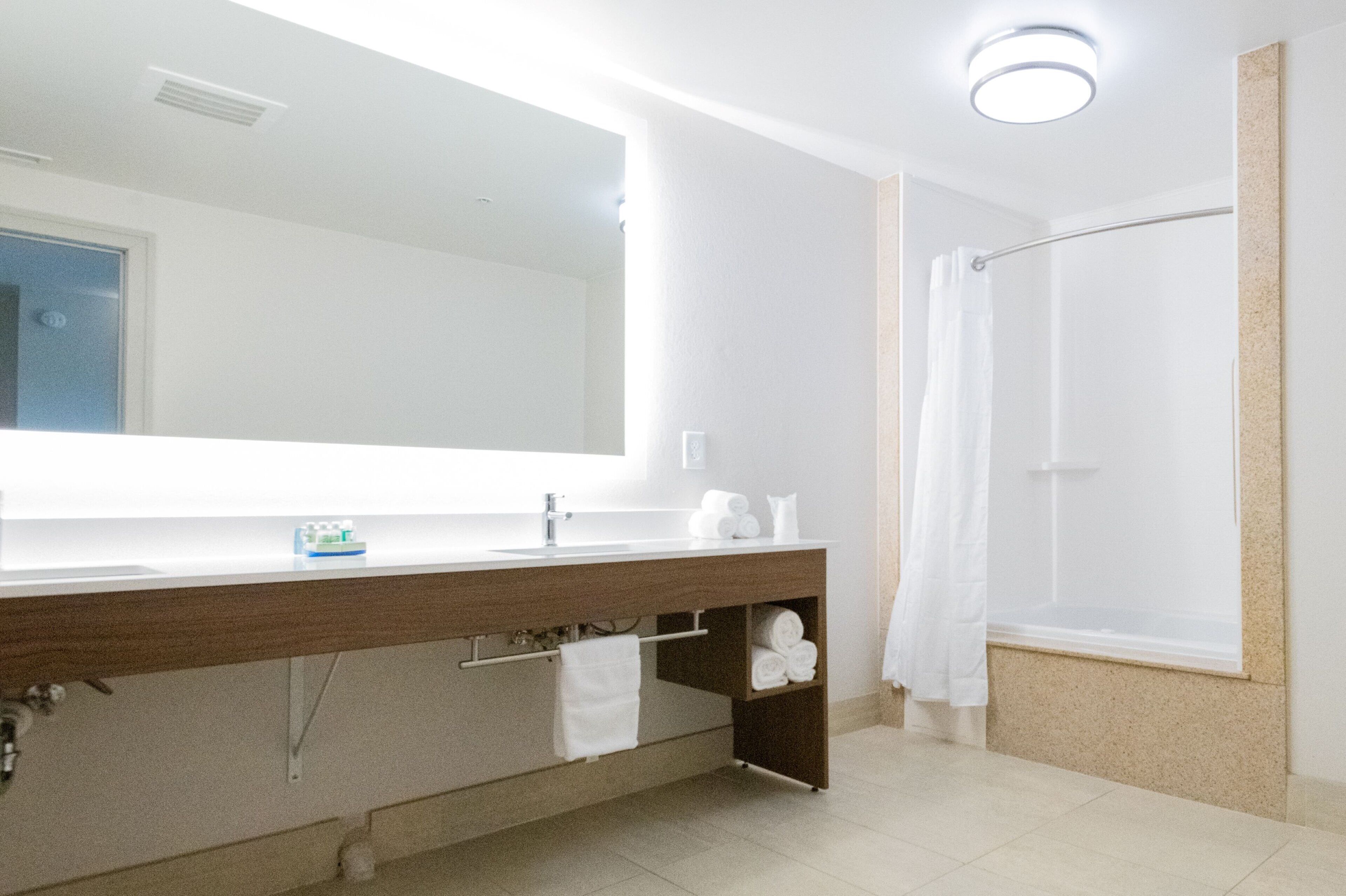 Une salle de bain moderne avec un grand miroir, un meuble-lavabo en bois, une douche avec rideau et un porte-serviettes.