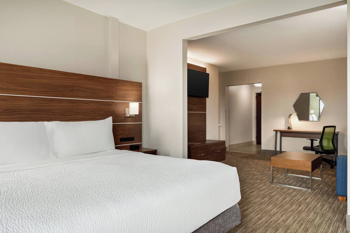 A hotel room with a large bed, a desk with a chair, a mirror, and a TV on the wall.