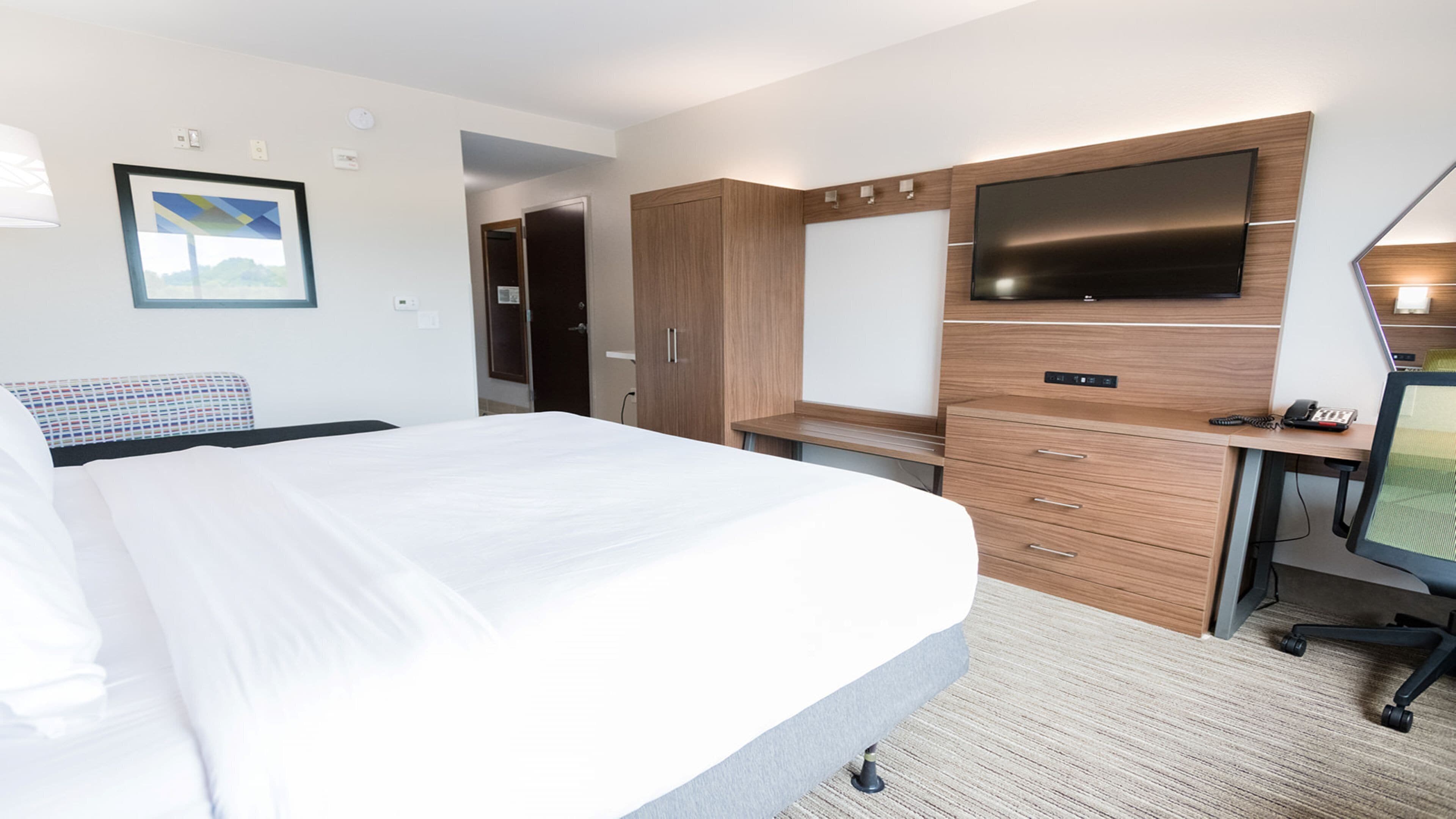 A hotel room with a bed, a desk with a computer, a TV, and a wardrobe.