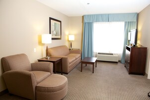 Una habitación de hotel con sofá, sillón y televisor sobre un mueble de madera.