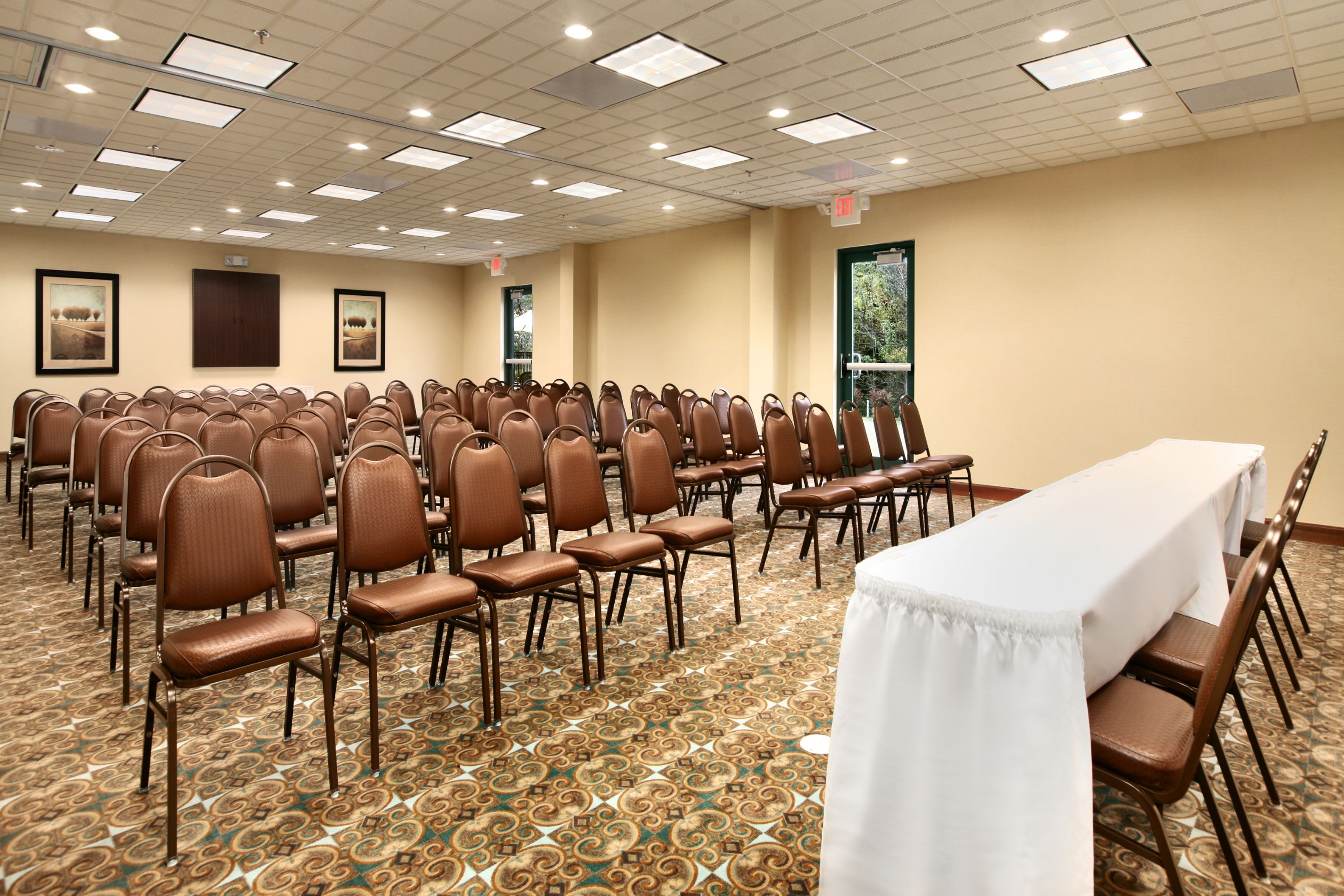 A conference room with rows of brown chairs, a long table with a white tablecloth, and patterned carpet.