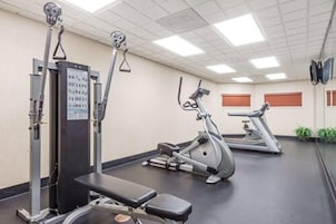 Un gimnasio con equipamiento de ejercicio, una banca y un espejo grande.
