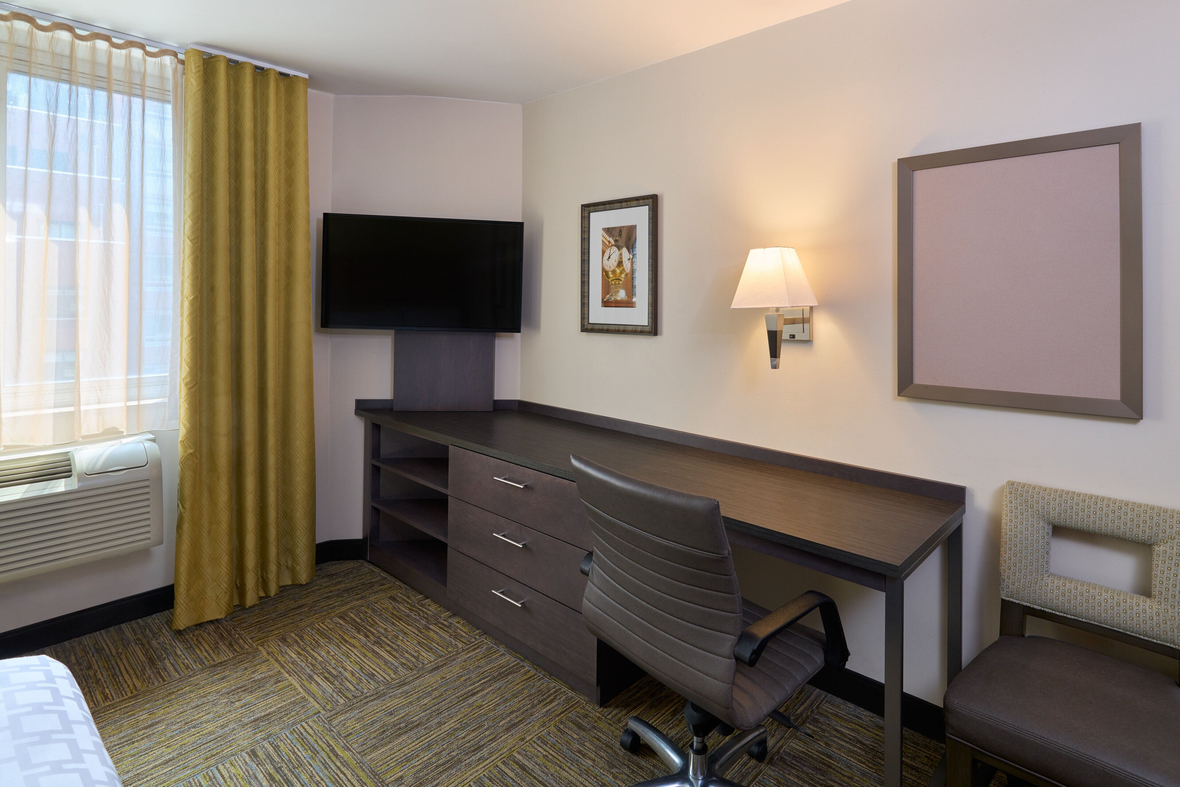 A hotel room with a desk, a chair, a television, a lamp, and a bed.