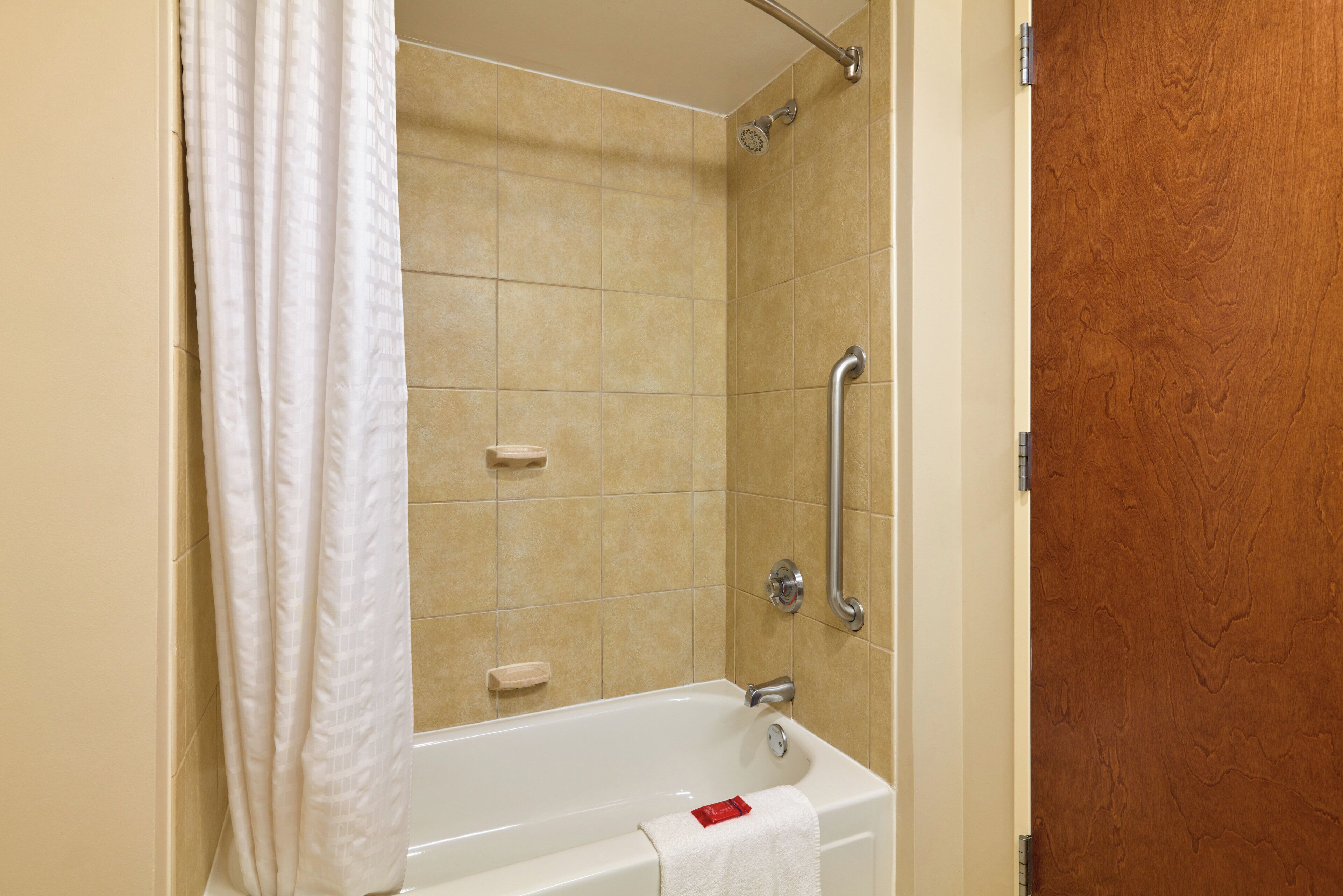 A bathroom with a bathtub, a shower, and a handrail.