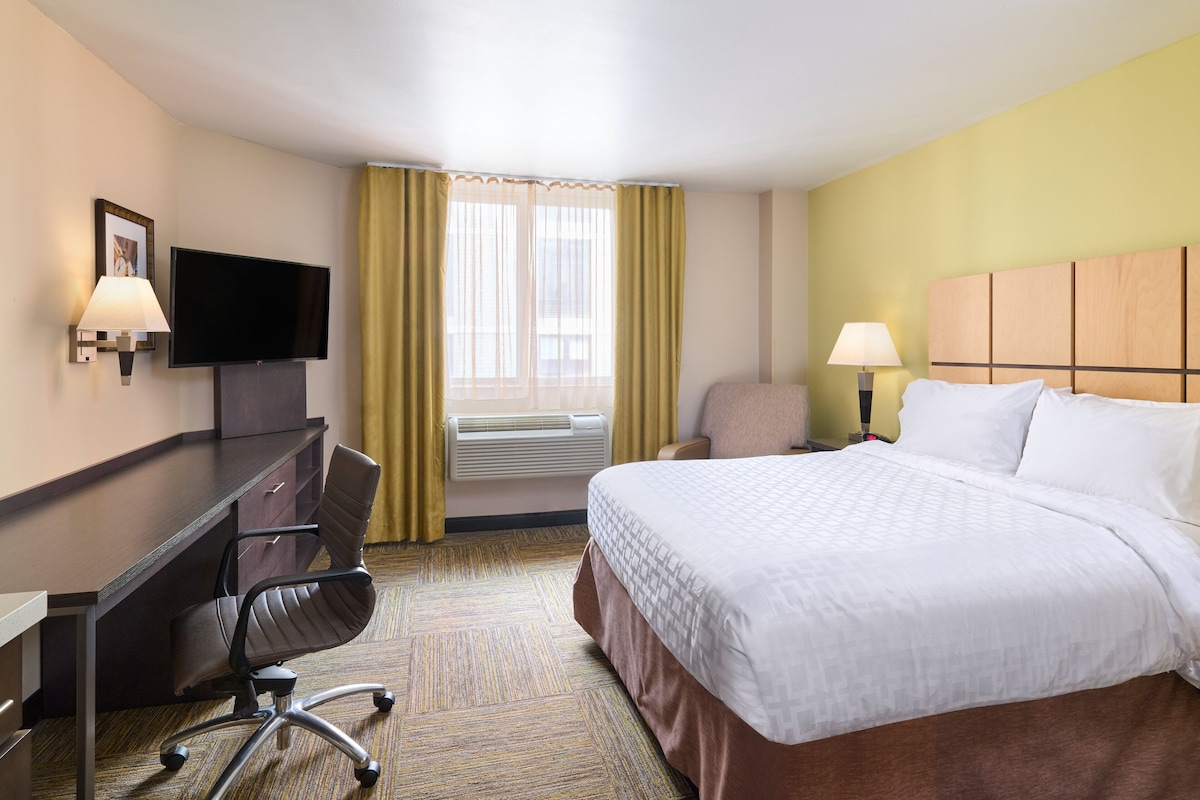 Habitación de hotel con cama, escritorio, silla, televisión y ventana con cortinas.
