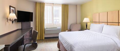 Habitación de hotel con cama, escritorio, silla, televisión y ventana con cortinas.