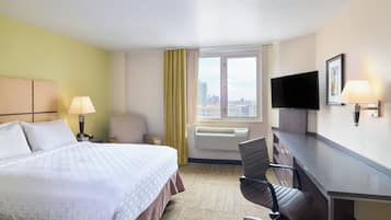 A hotel room with a bed, a desk, a chair, a television, and a window with a city view.