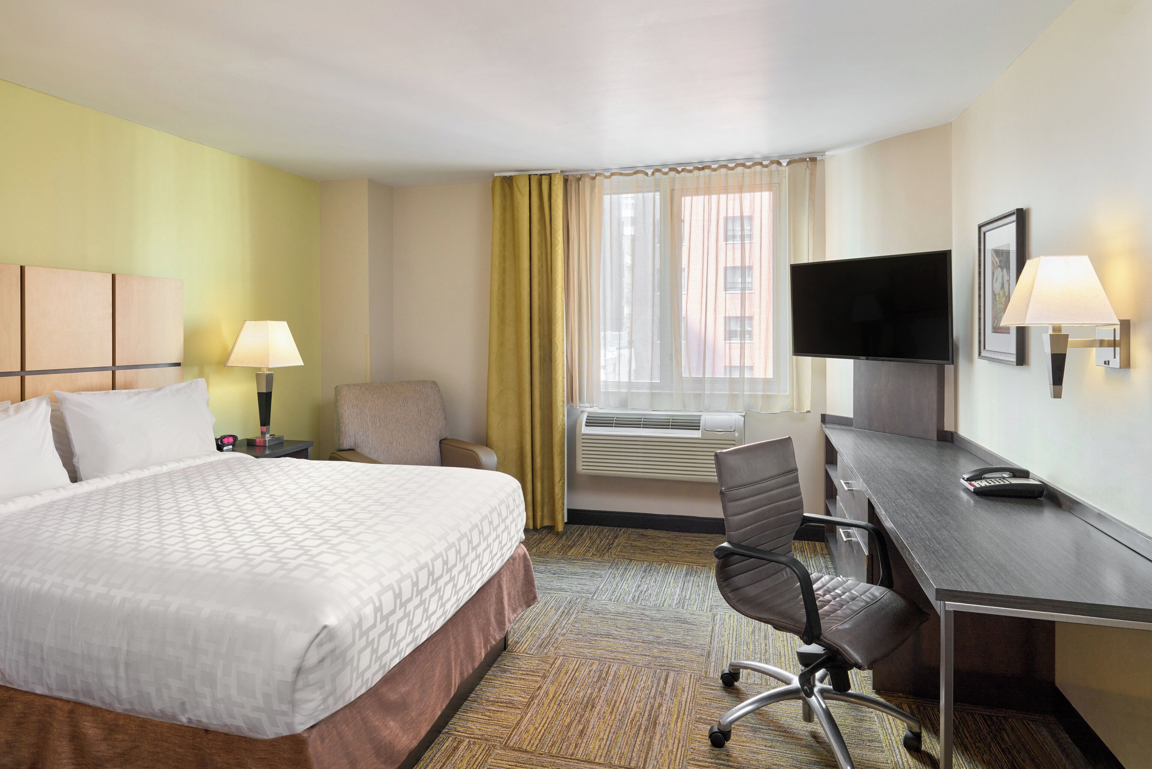 Une chambre d’hôtel équipée d’un lit, d’un bureau, d’une chaise, d’une télévision et d’un appareil de climatisation.