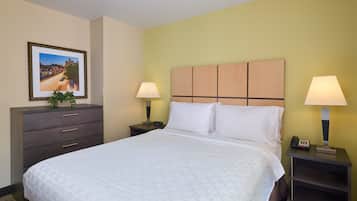 Habitación de hotel con una cama grande, dos mesitas de noche, un tocador, un aparador, un cuadro enmarcado en la pared y una planta en maceta.