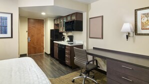 A hotel room with a bed, a desk, a chair, a microwave, a coffee maker, and a clock on the wall.