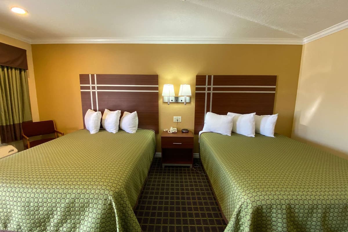 Une chambre d’hôtel avec deux lits, une table de chevet avec un téléphone et des lampes fixées au mur.