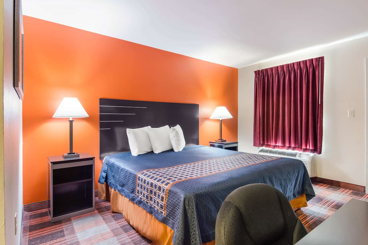 A hotel room with a bed, two bedside tables with lamps, a window with curtains, and a carpeted floor.