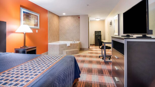 A hotel room with a bed, a desk, a television, a bathroom with a bathtub, and a painting on the wall. - Americas Best Value Inn & Suites Mableton Atlanta (Mableton)