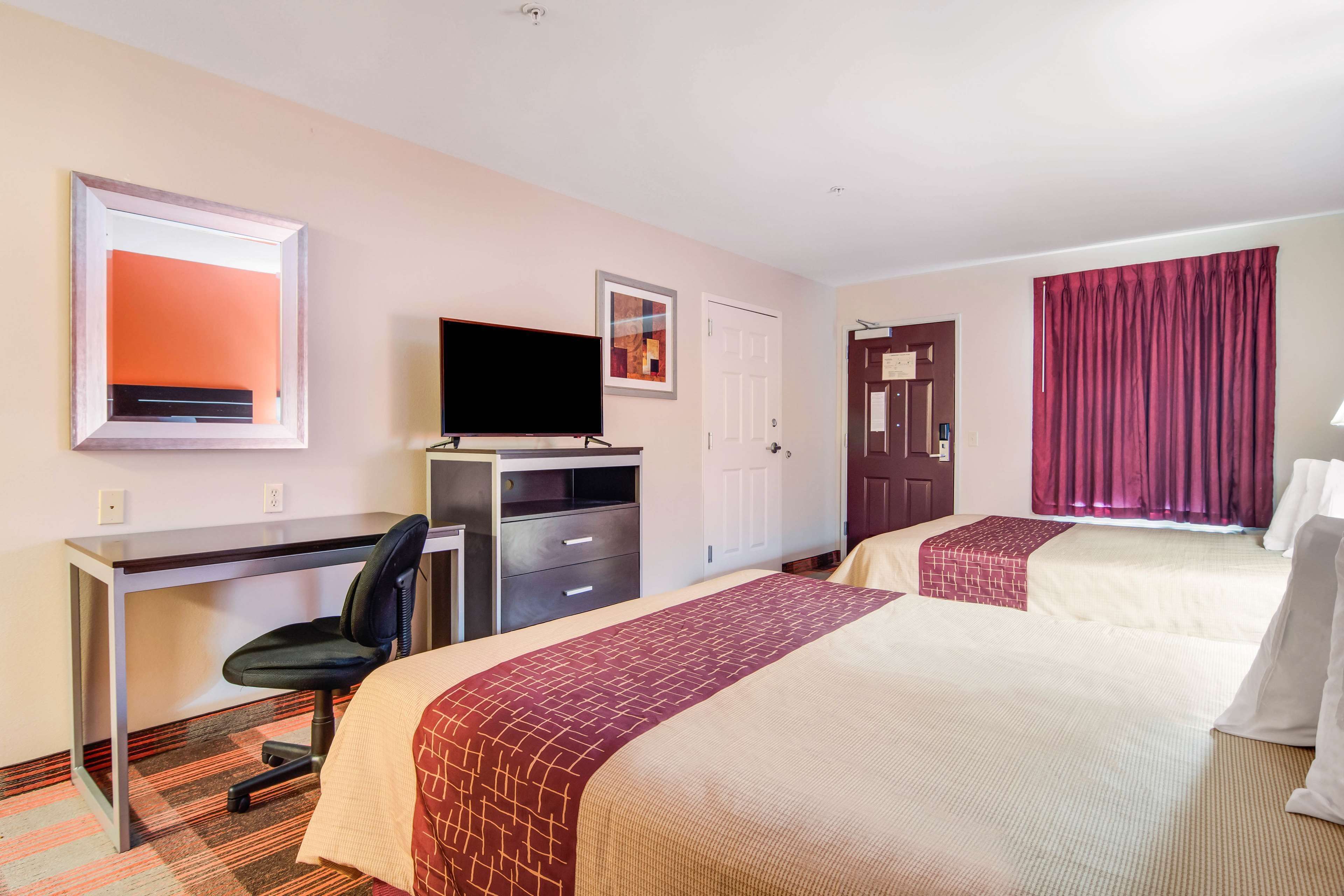 Habitación de hotel con dos camas, un escritorio con silla, un televisor y una ventana con cortinas.