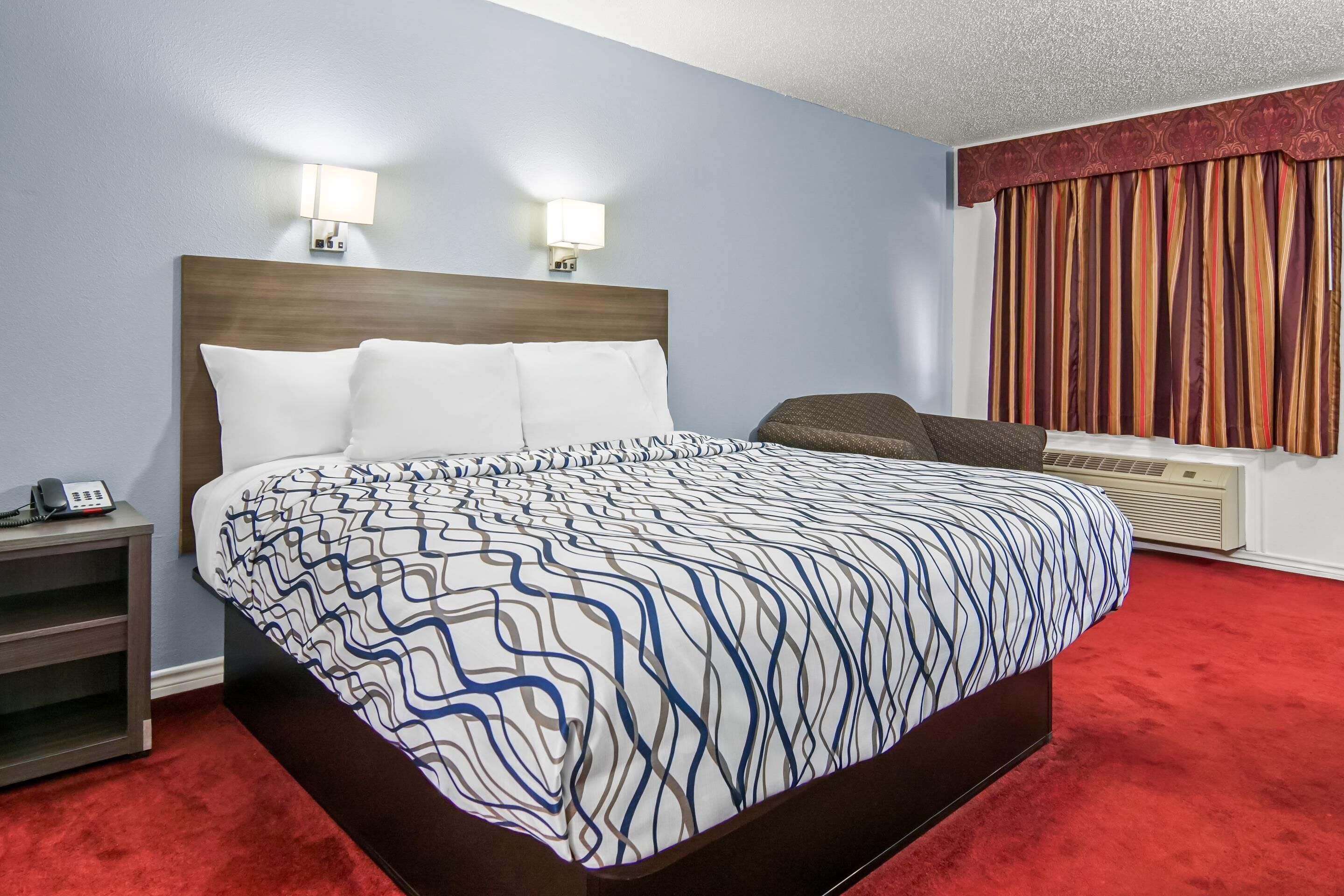 Habitación de hotel con cama, lámparas de noche, teléfono, una silla y ventana con cortinas.