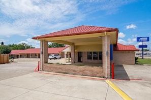 A motel with a red roof, brick exterior, and a covered parking area. - Americas Best Value Inn Weatherford, TX (Weatherford)