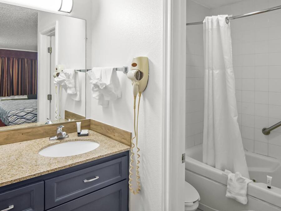 Un baño con lavamanos, espejo, perchero para toallas, secador de pelo y cortina de ducha.