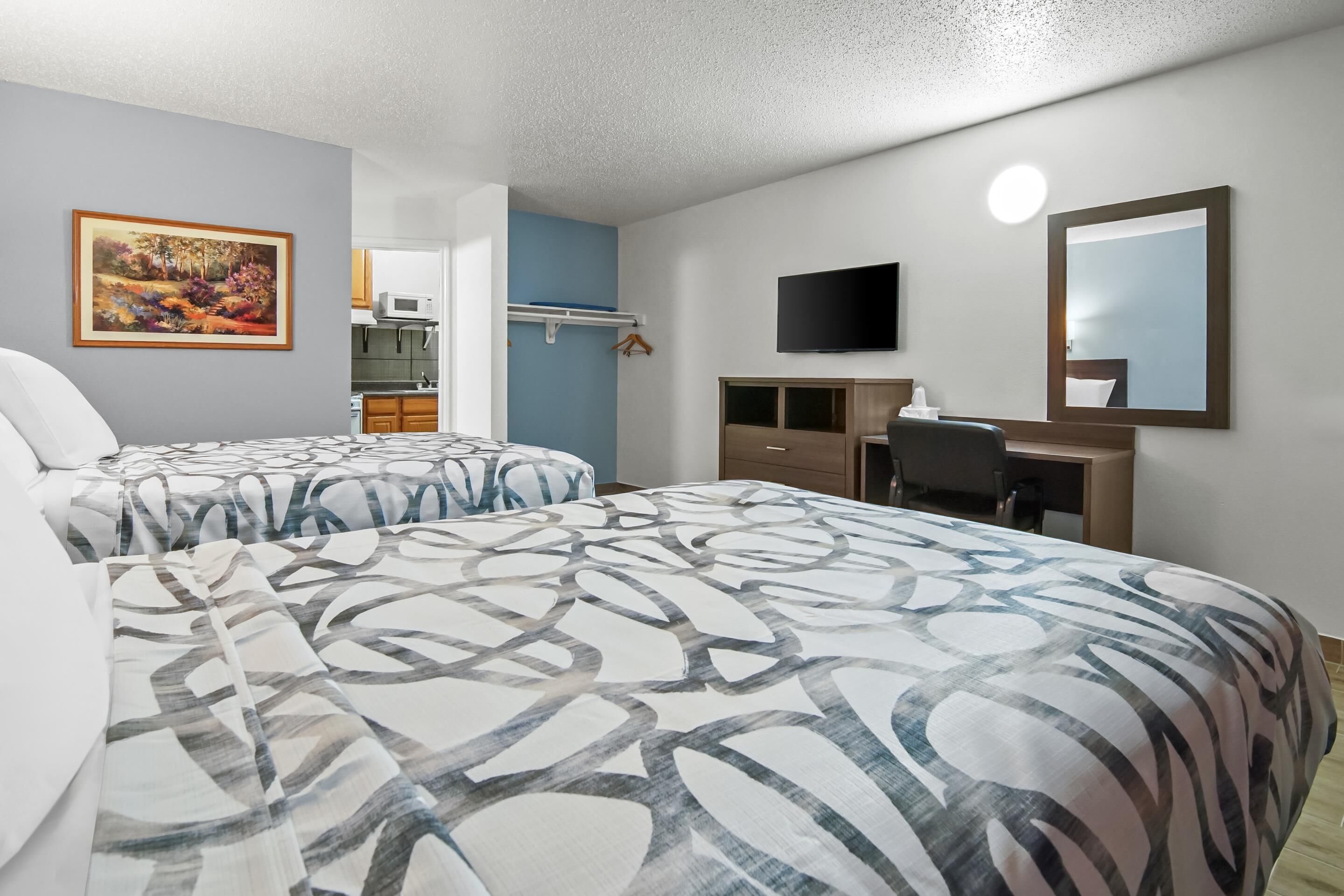 A hotel room with two beds, a TV, a desk, a mirror, and a painting on the wall.