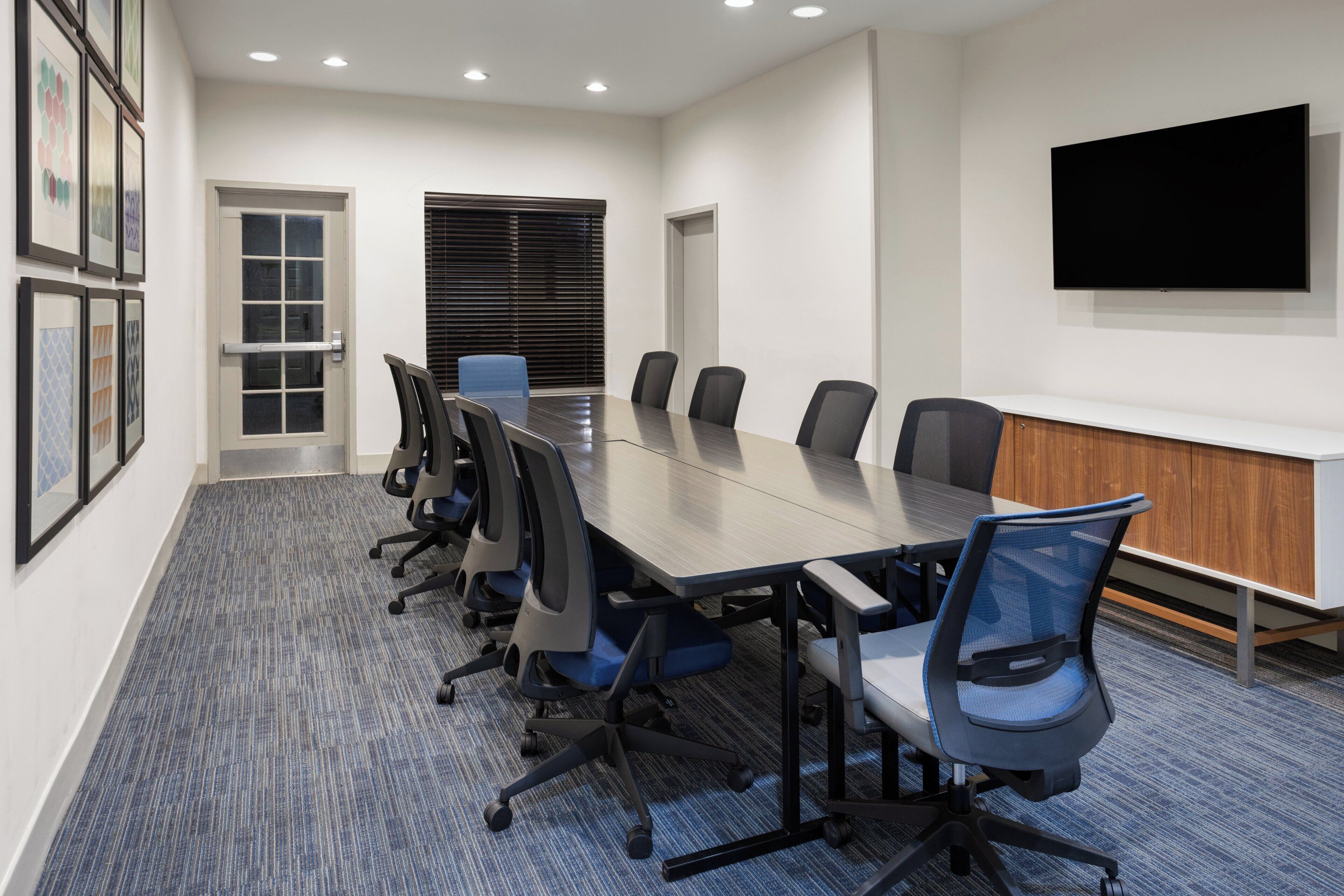 A conference room with a long table, six chairs, a TV on the wall, and framed pictures on the wall.