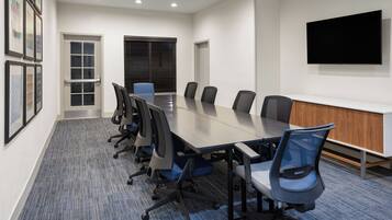 A conference room with a long table, six chairs, a TV on the wall, and framed pictures on the wall.