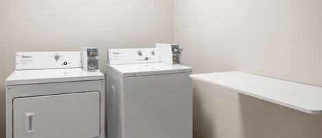 Une buanderie équipée de deux machines à laver et deux sèche-linge superposés, d’une étagère blanche et d’un mur sobre.