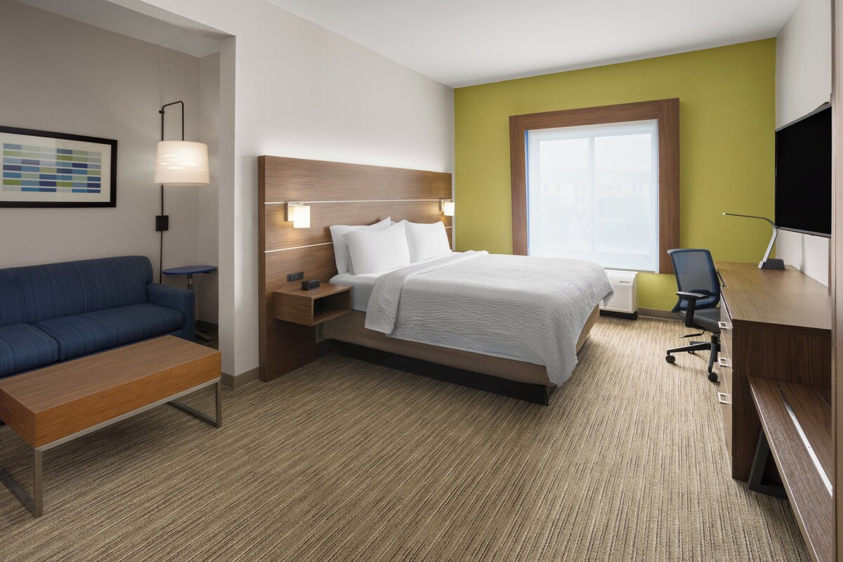 Quarto de hotel com cama, escrivaninha, cadeira, sofá e abajur.